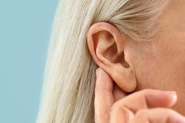 Ältere Dame hält sich den Finger ans Ohr, als ob sie schlecht hören würde.