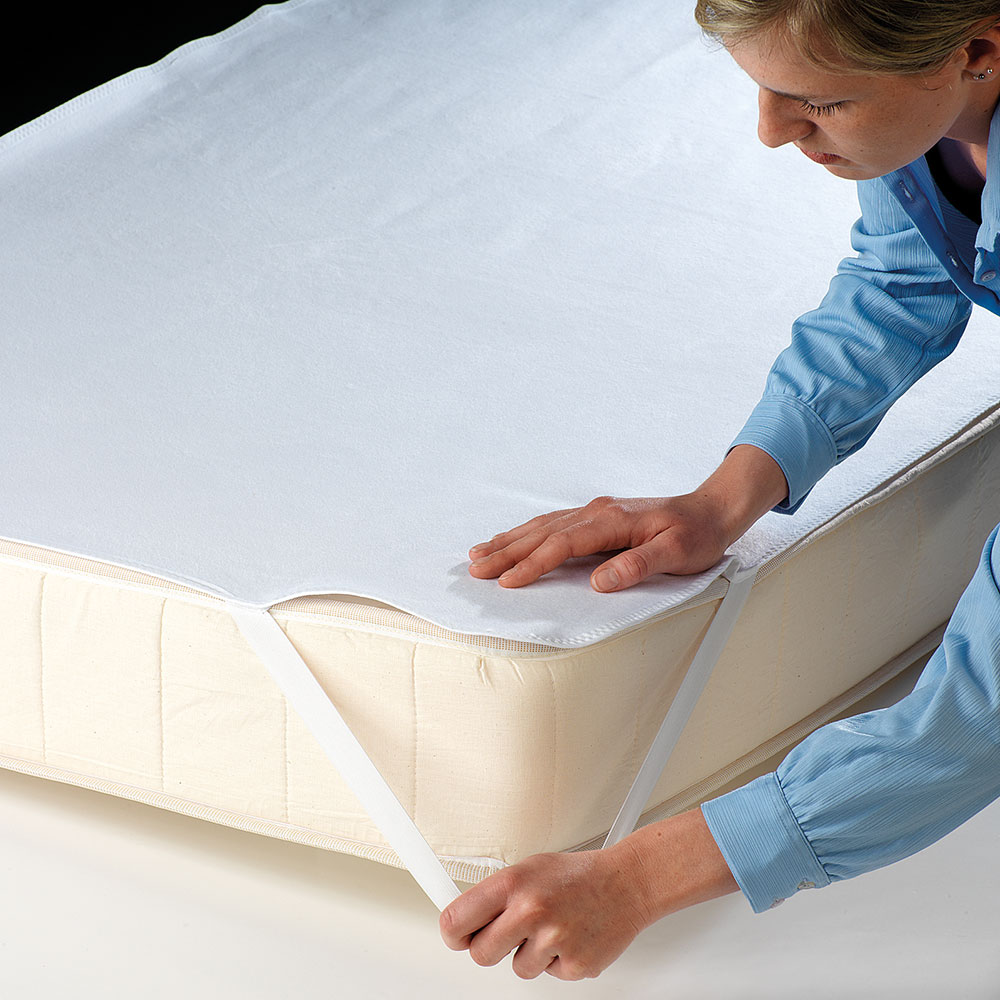 Frau bezieht Bett mit einer wasserdichten Matratzenauflage/ Inkontinenzauflage