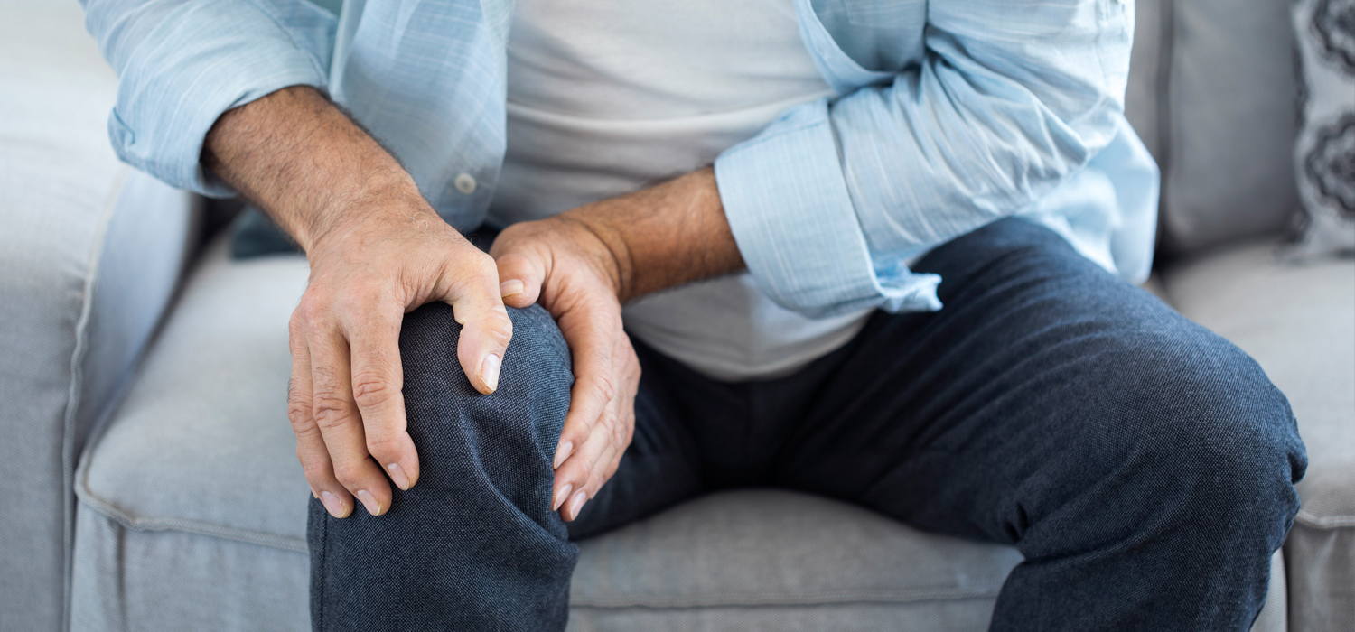 Mann fasst sich mit beiden Händen ans Knie, da er Knieschmerzen zu haben scheint.