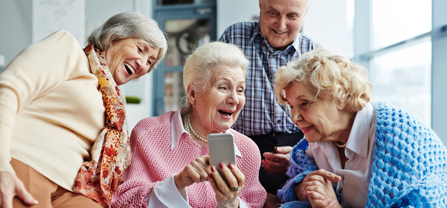 Eine Gruppe älterer Damen schaut belustigt auf ein Mobiltelefon.