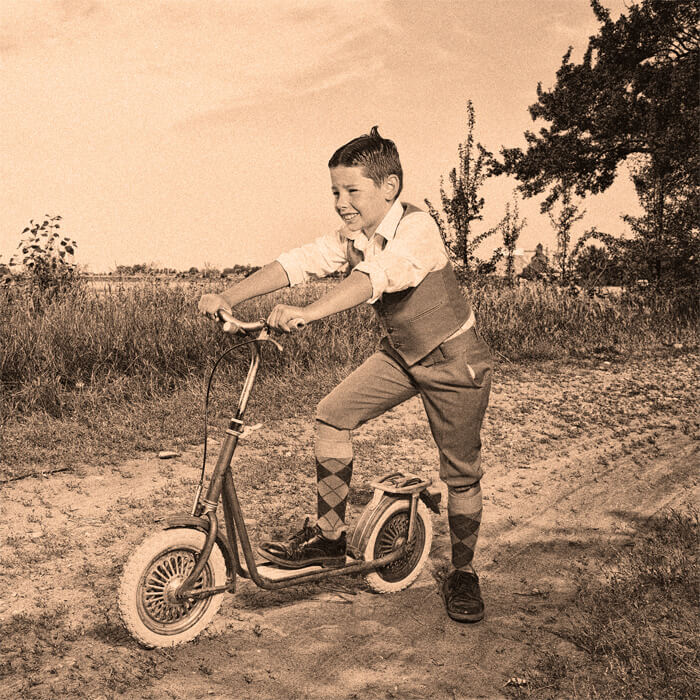 Historische Darstellung eines Jungen, der Freude am Fahren eines Tretrollers hat.