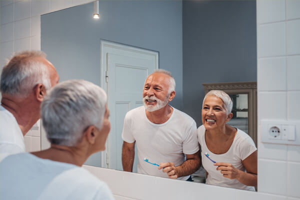 Älteres Ehepaar putzt sich gemeinsam die Zähne im Badezimmer vorm Spiegel und sieht glücklich aus.