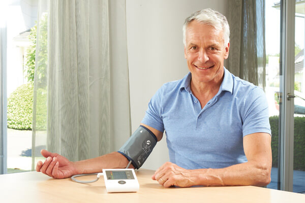 Älterer Mann misst mittels Blutdruckmessgerät seinen Blutdruck.