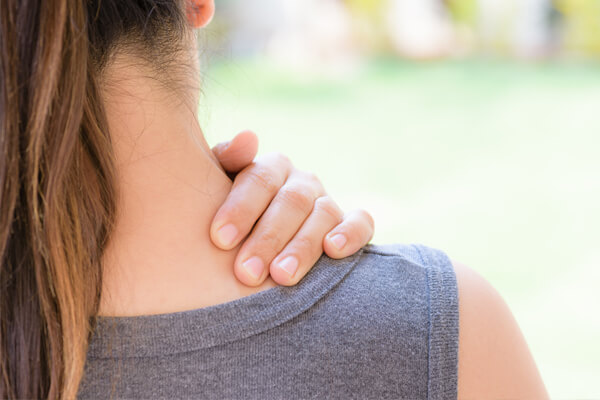 Man sieht die Schulter einer Frau, die Nackenschmerzen hat und sich mit der linken Hand an den Nacken fasst.
